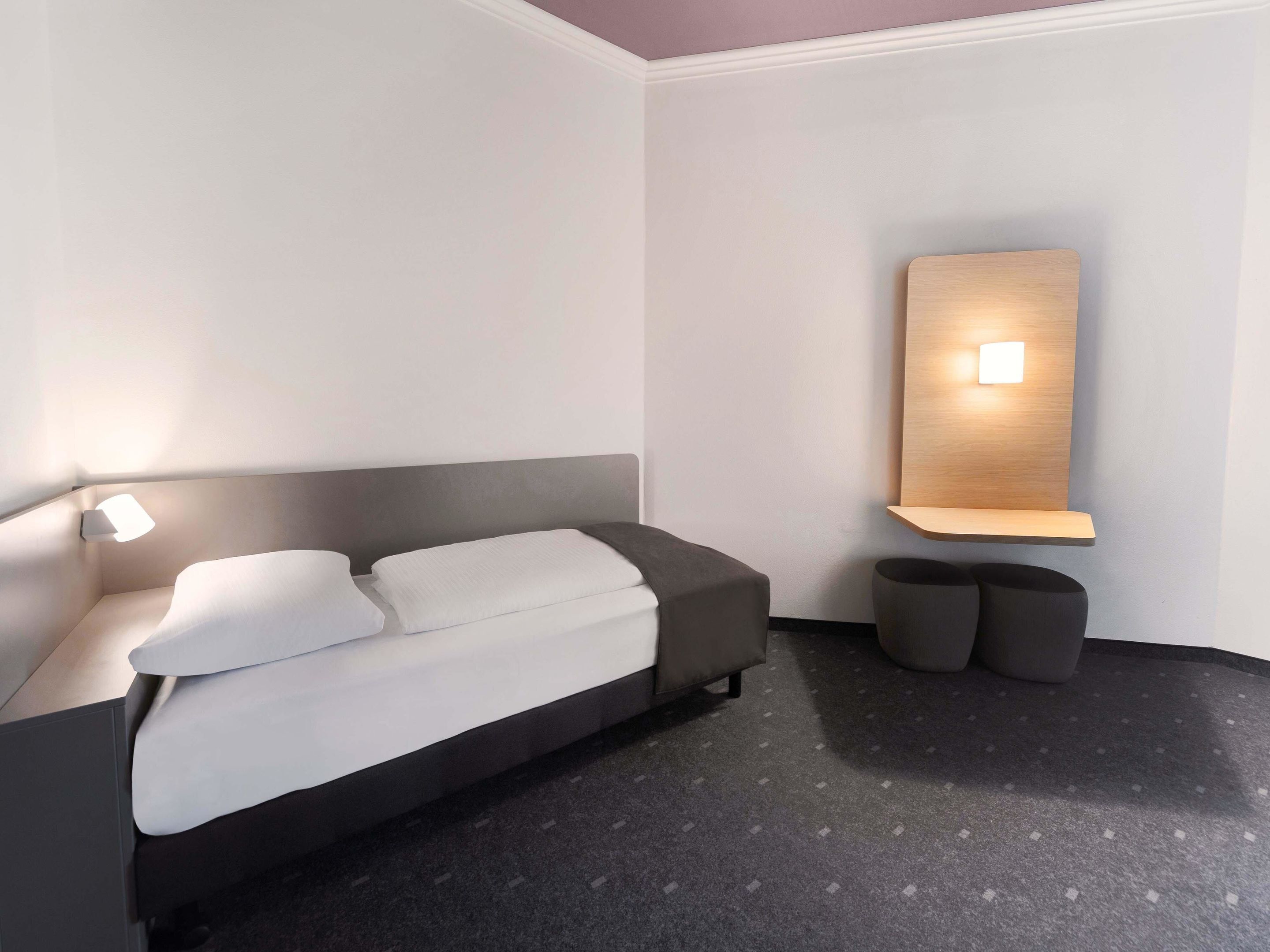 Un dormitorio moderno con cama, lámparas de noche, estante en la pared y una mesita redonda.