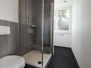 Ein modernes Badezimmer mit einer Glaskabine zur Dusche, einer weißen Toilette und einem Fenster, das für natürliches Licht sorgt.