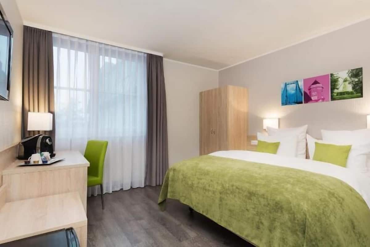 Habitación de hotel con cama, escritorio, silla, armario y cuadros en la pared.