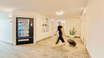 A hallway with a vending machine, a framed picture, and a potted plant.