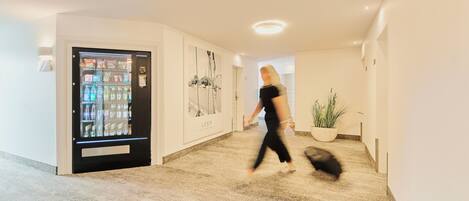 A hallway with a vending machine, a framed picture, and a potted plant.