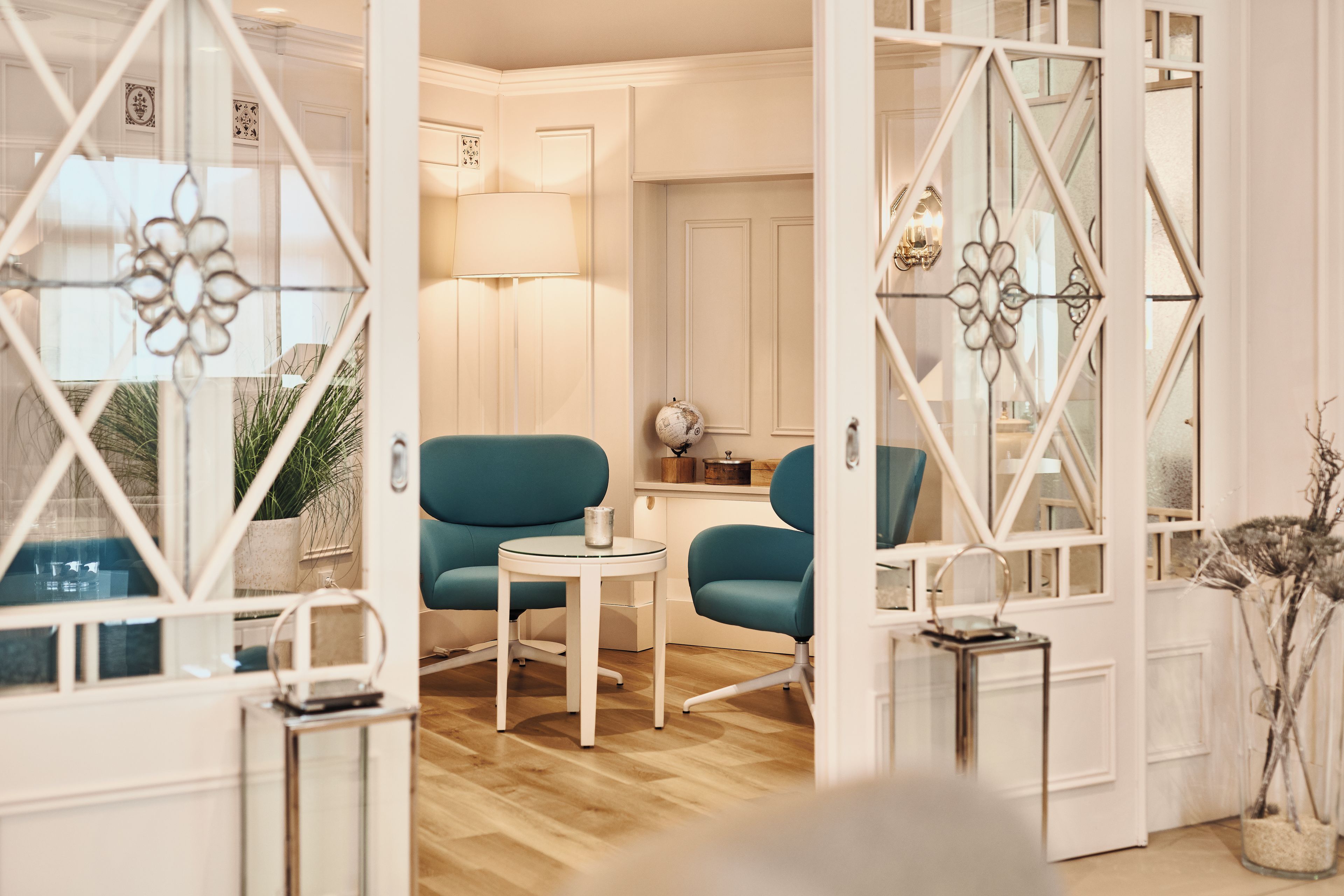 A room with a teal armchair, a small round table, and a globe on a shelf.