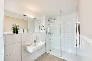 Un baño moderno con ducha envuelta en vidrio, un lavabo blanco y un espejo encima.