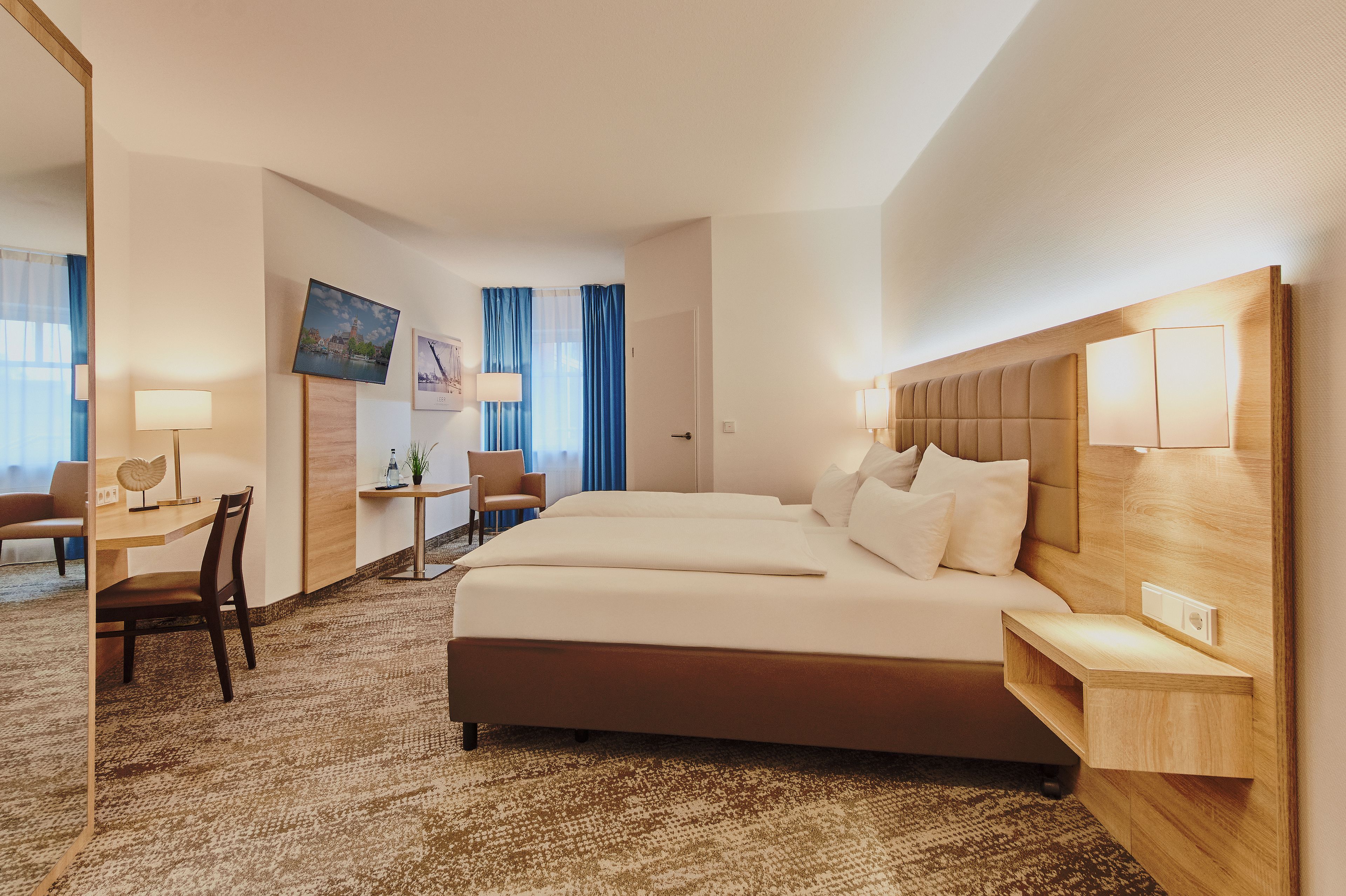 A hotel room with a large bed, a desk, a chair, a TV, and a window with curtains.
