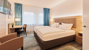 Habitación de hotel con cama, escritorio, silla, lámpara y vista al exterior.