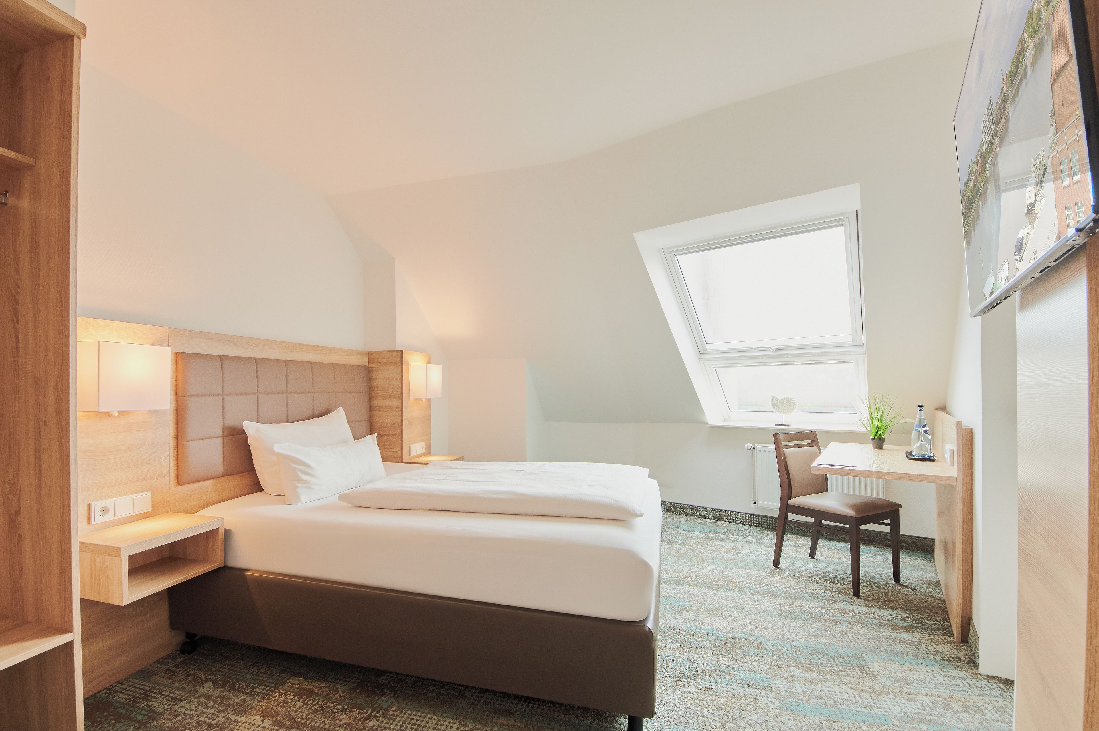 Ein Hotelzimmer mit Bett, Nachttisch, Sessel, Schreibtisch und Fenster.