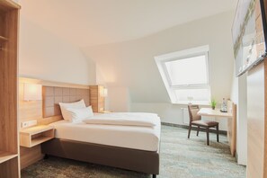 Una habitación de hotel con cama, mesita de noche, silla, escritorio y ventana.