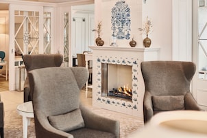 A living room with two armchairs, a fireplace with a tiled surround, and a decorative wall piece above the mantel.
