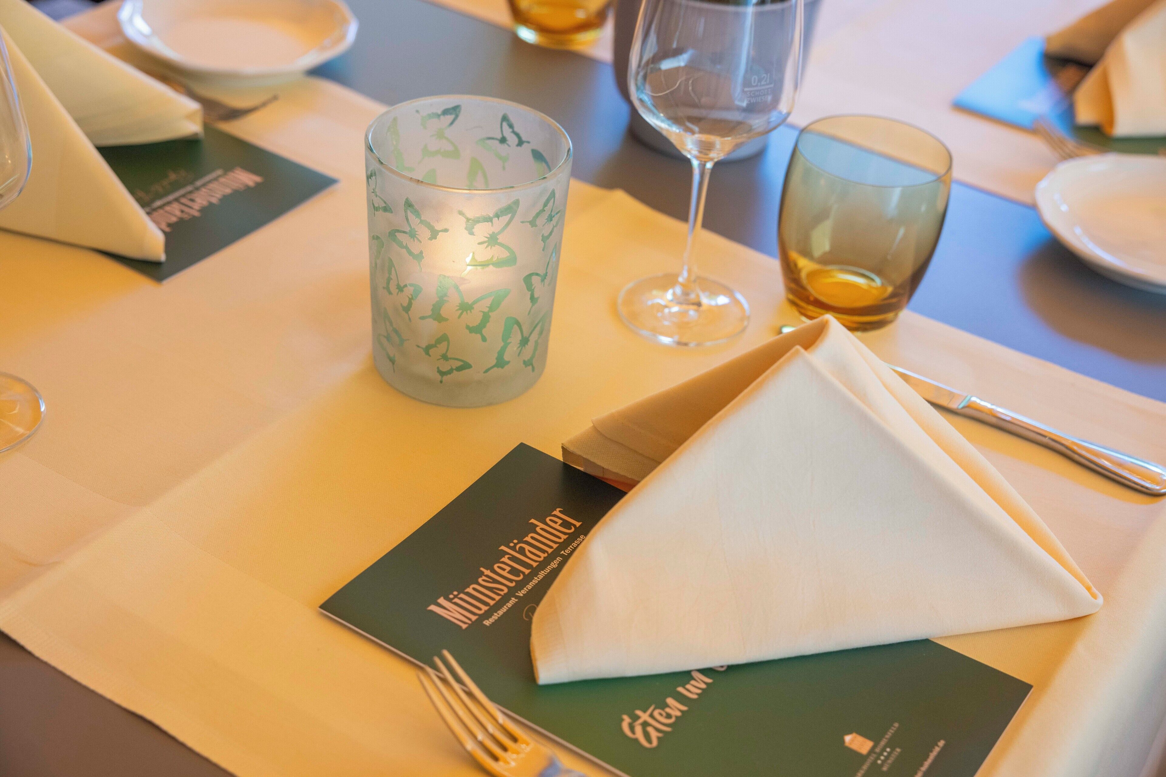 Een gedekte tafel met een menukaart, een kaars, een glas water en een gevouwen servet.