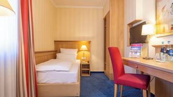 Quarto de hotel com cama, escrivaninha, cadeira, televisão e abajur.