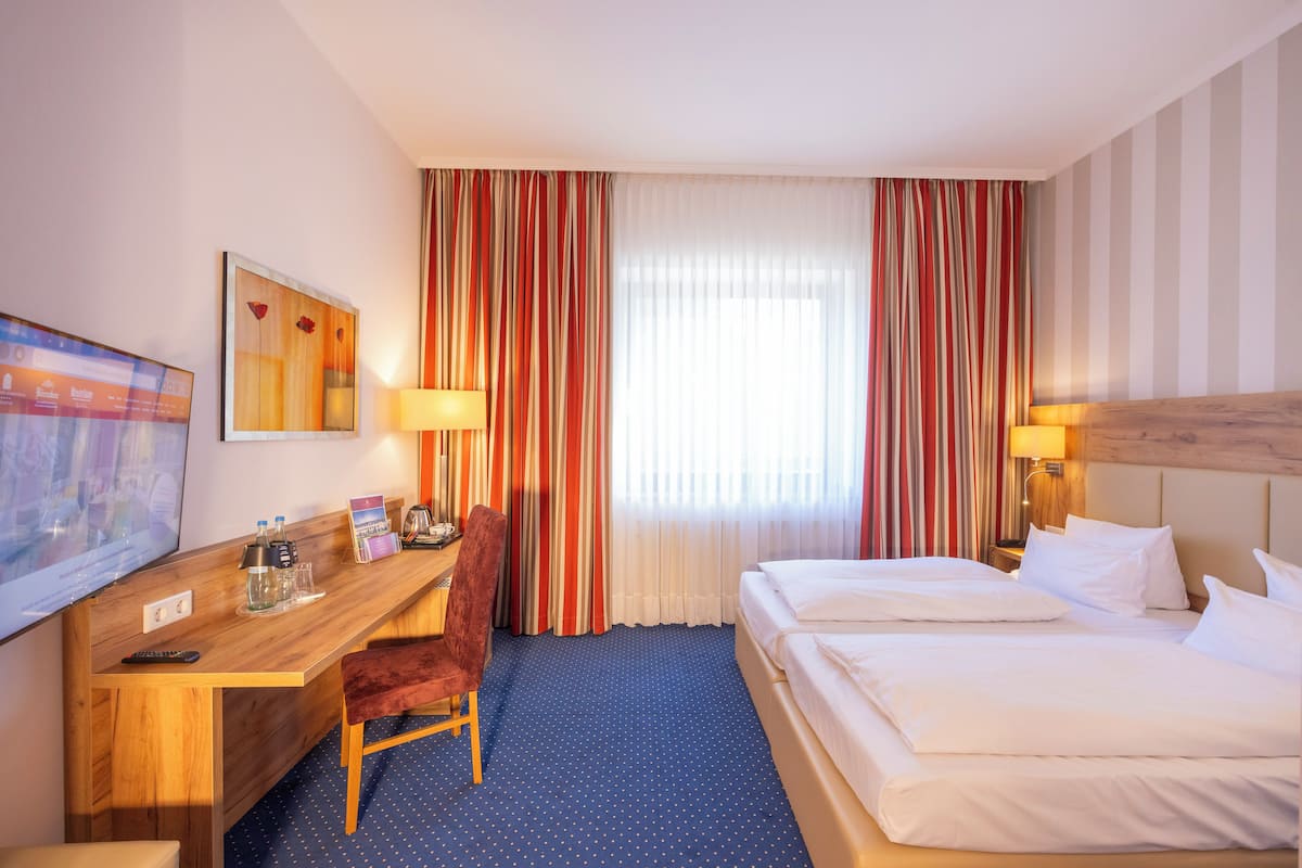 A hotel room with a wooden desk, a chair, a bed, and a large window with striped curtains.