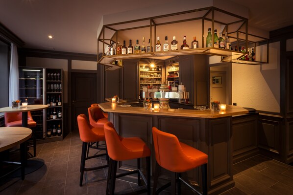 Una zona de bar con mostrador de madera, taburetes naranjas y estantes llenos de botellas.