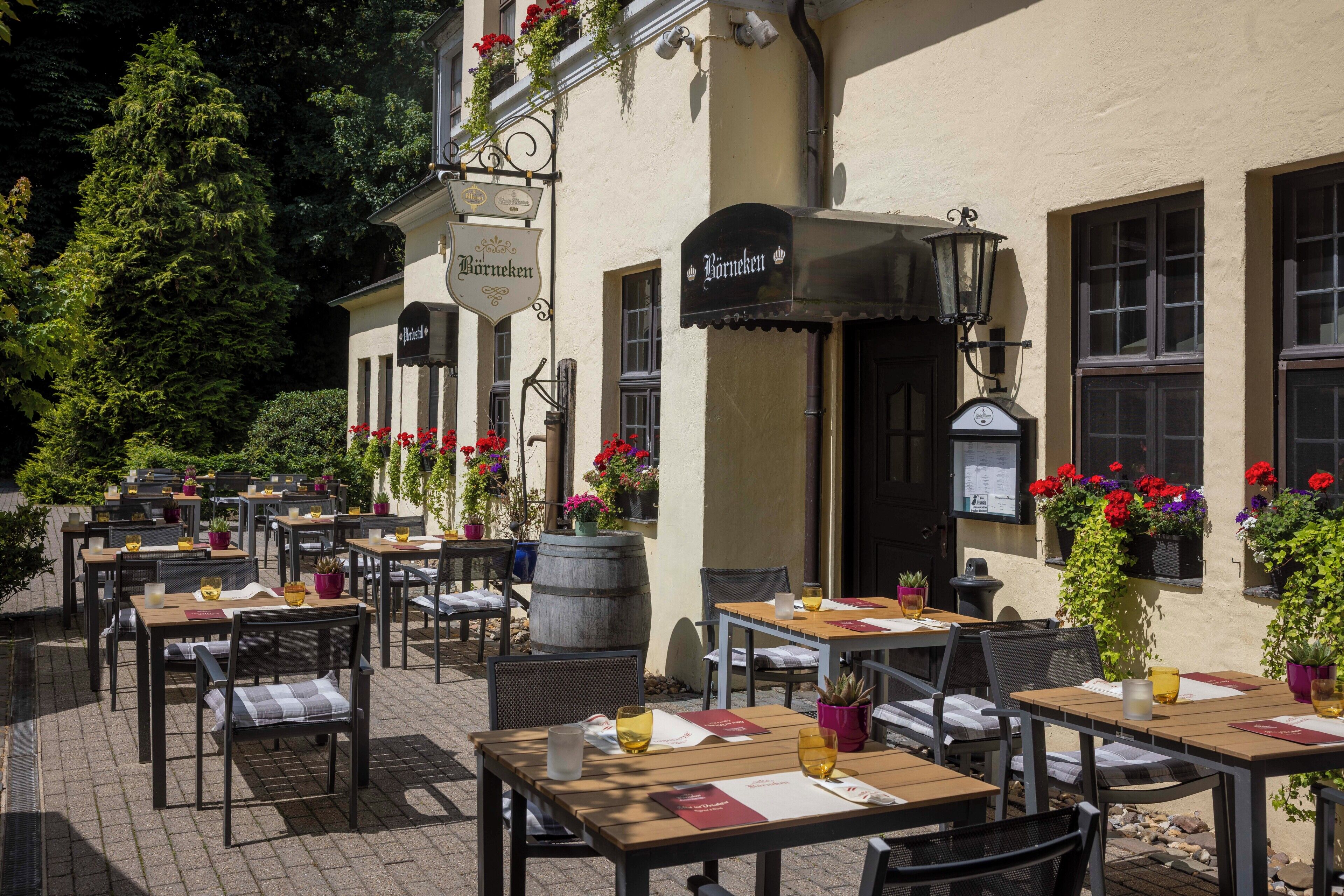 An outdoor seating area with tables and chairs, potted plants, and a building with a sign.