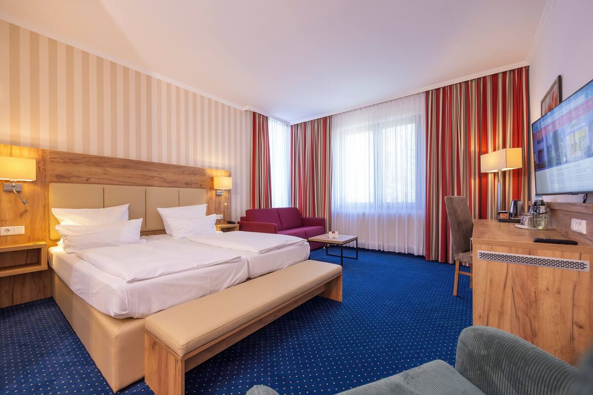 A hotel room with a large bed, a desk, a chair, a sofa, and a television.