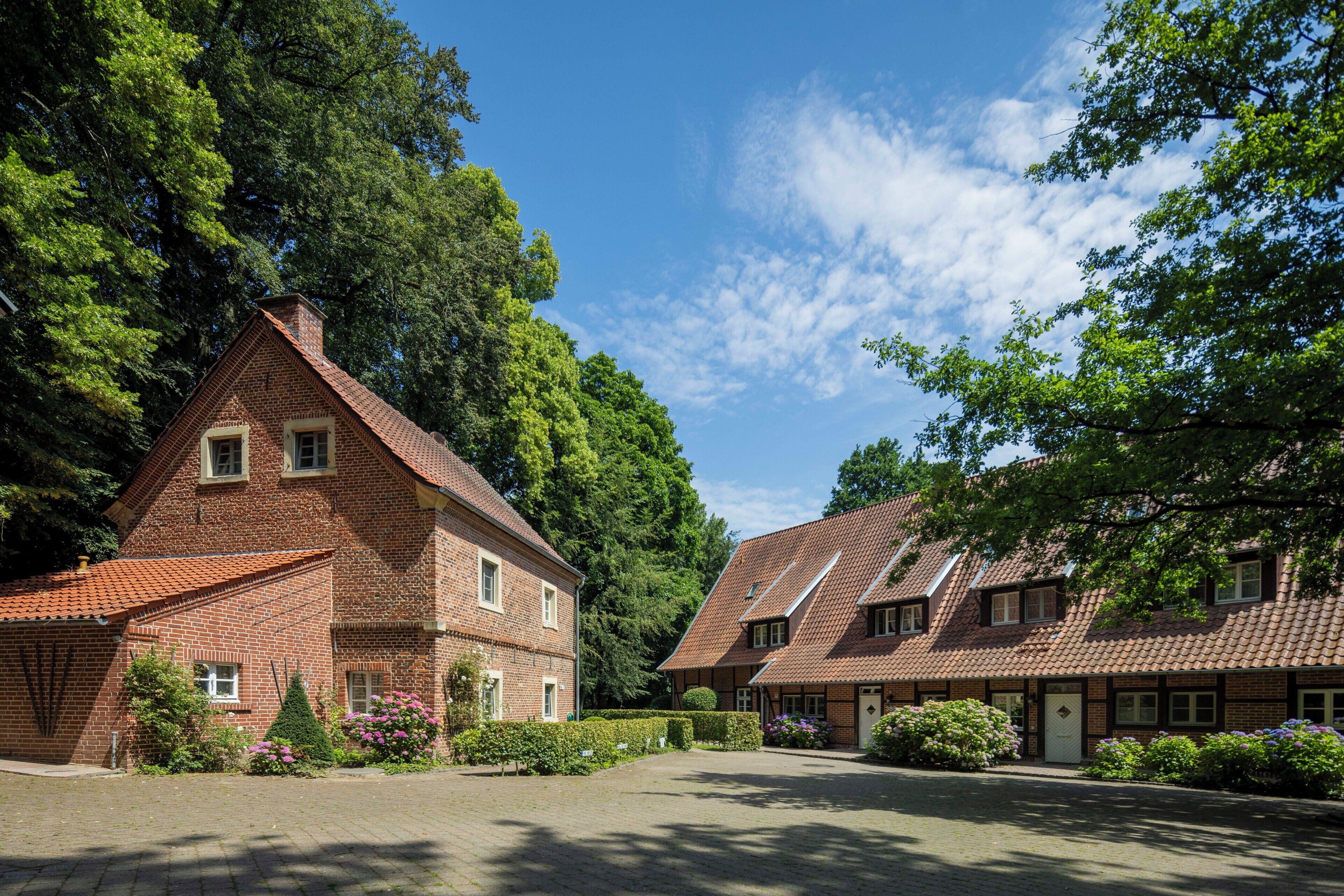 A traditional brick building with a symmetrical facade, a central entrance, and a paved courtyard.