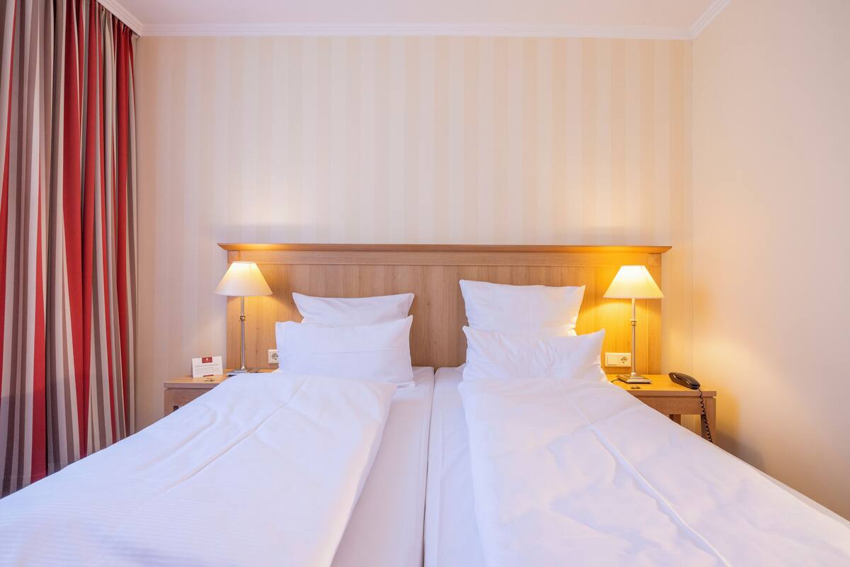 A double bed with white linens, two bedside lamps, and a wooden headboard.