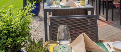 Un área de comedor al aire libre con mesas, sillas y plantas en macetas.