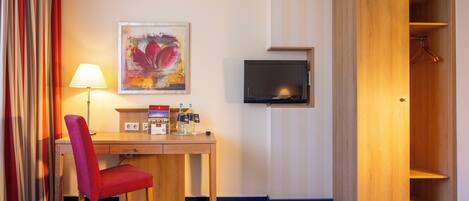 A hotel room with a desk, chair, TV, and wardrobe.