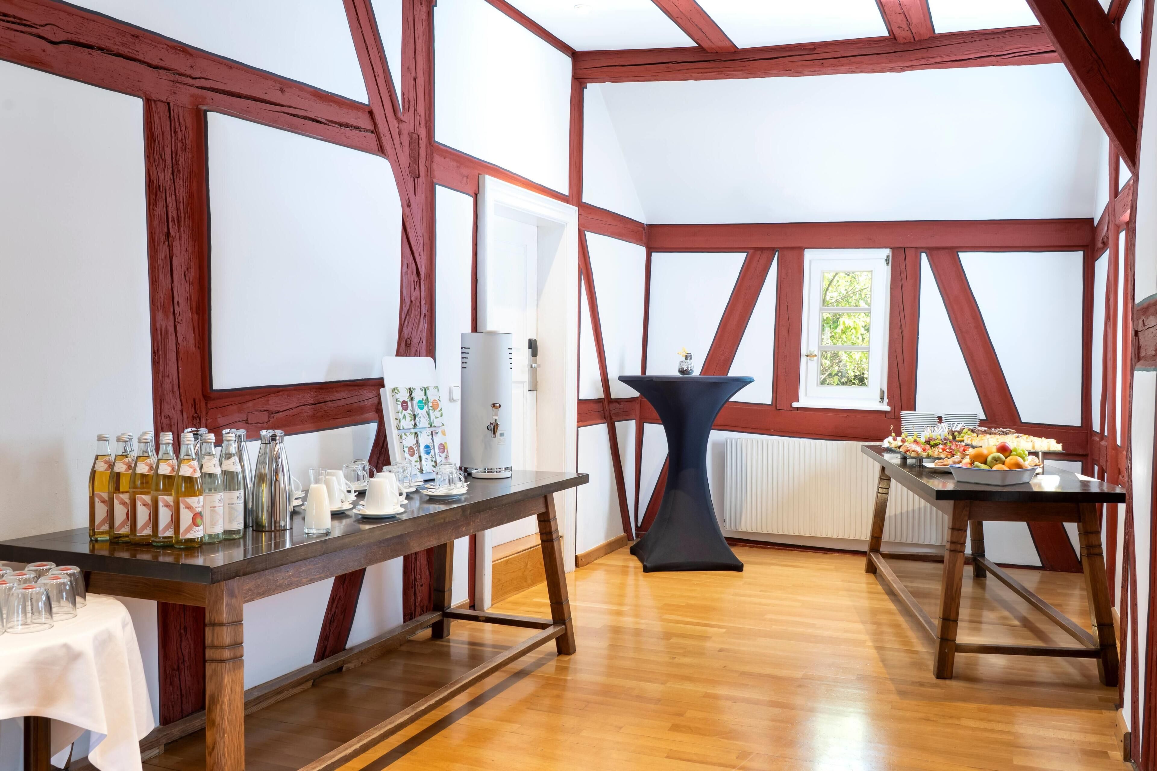 Ein Zimmer mit Holzbalken, einem Tisch mit Speisen und Getränken sowie einer Kaffeemaschine.