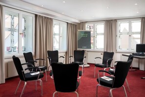Une salle de conférence avec des chaises noires, un écran de projection et une moquette rouge.