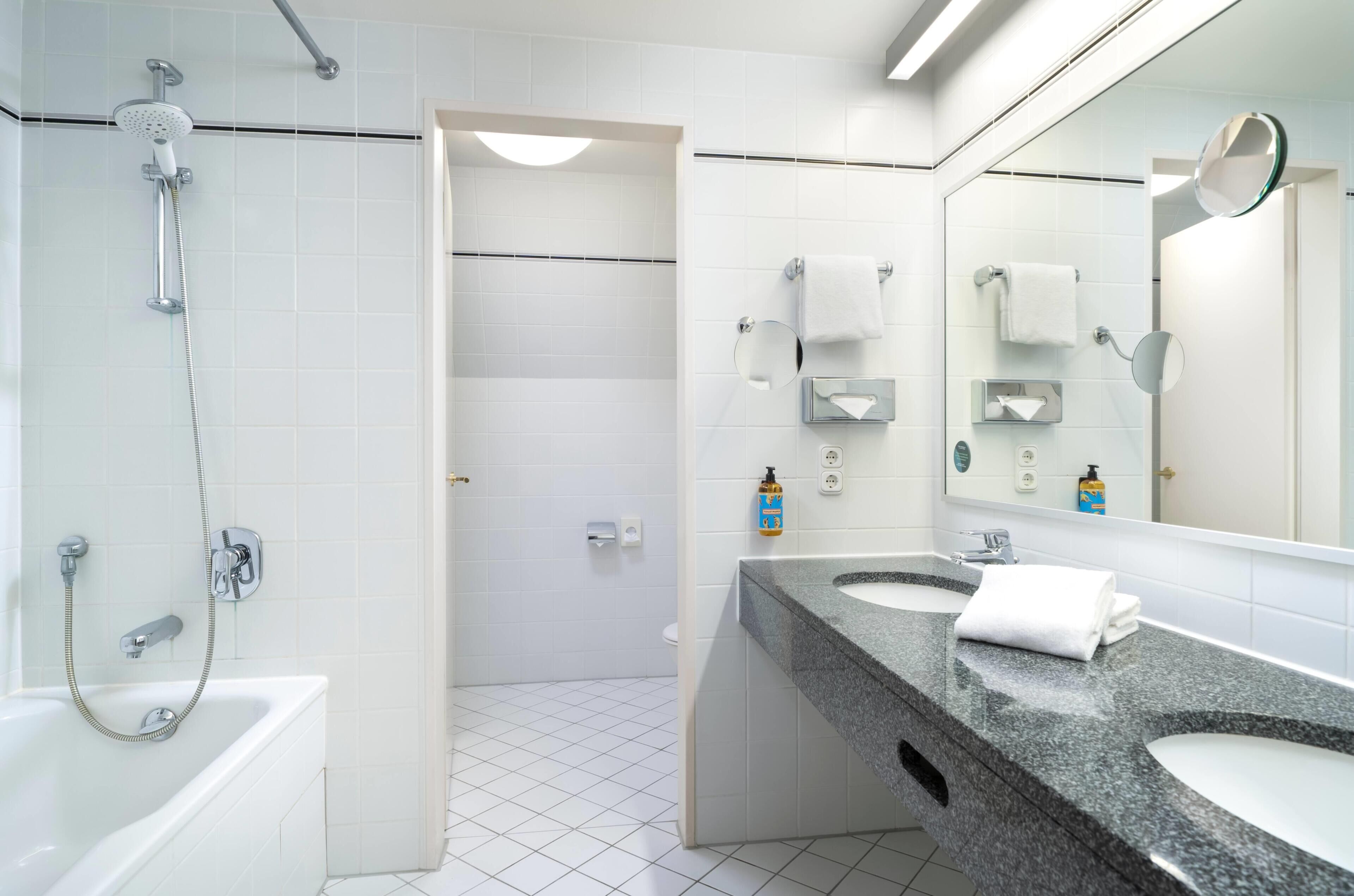 Un baño moderno con ducha, dos lavamanos, inodoro y un espejo grande.