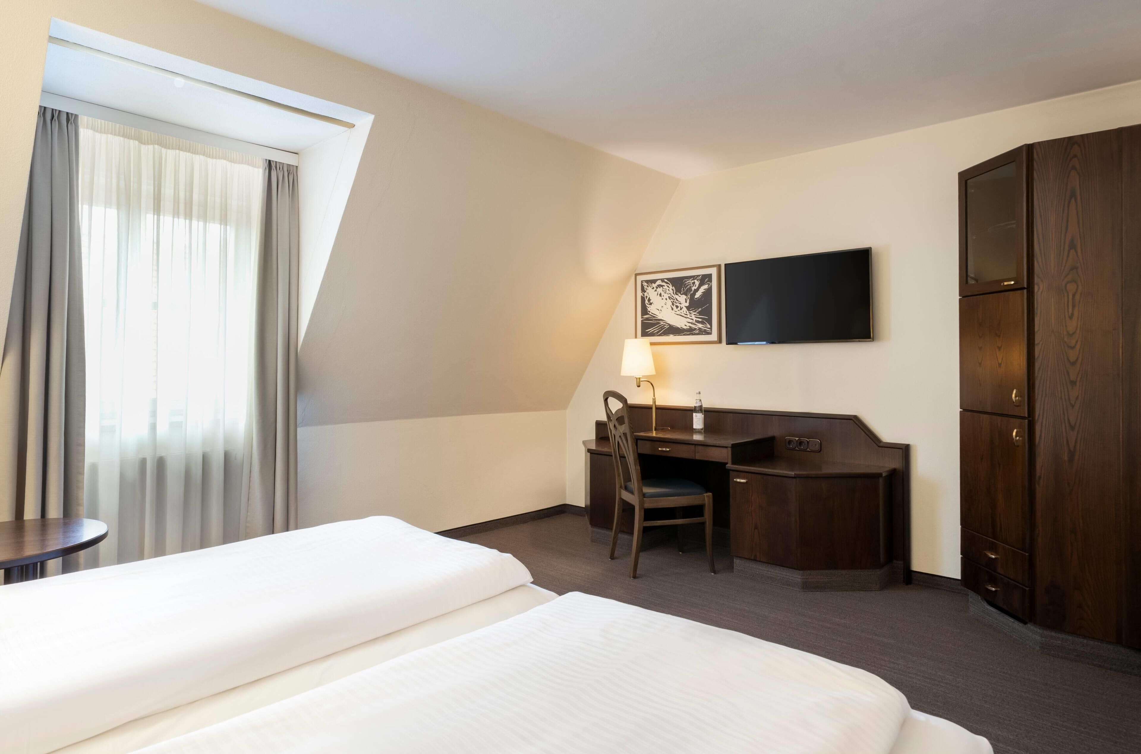 Habitació d'hotel amb llit, escriptori, cadira, televisió i armari.
