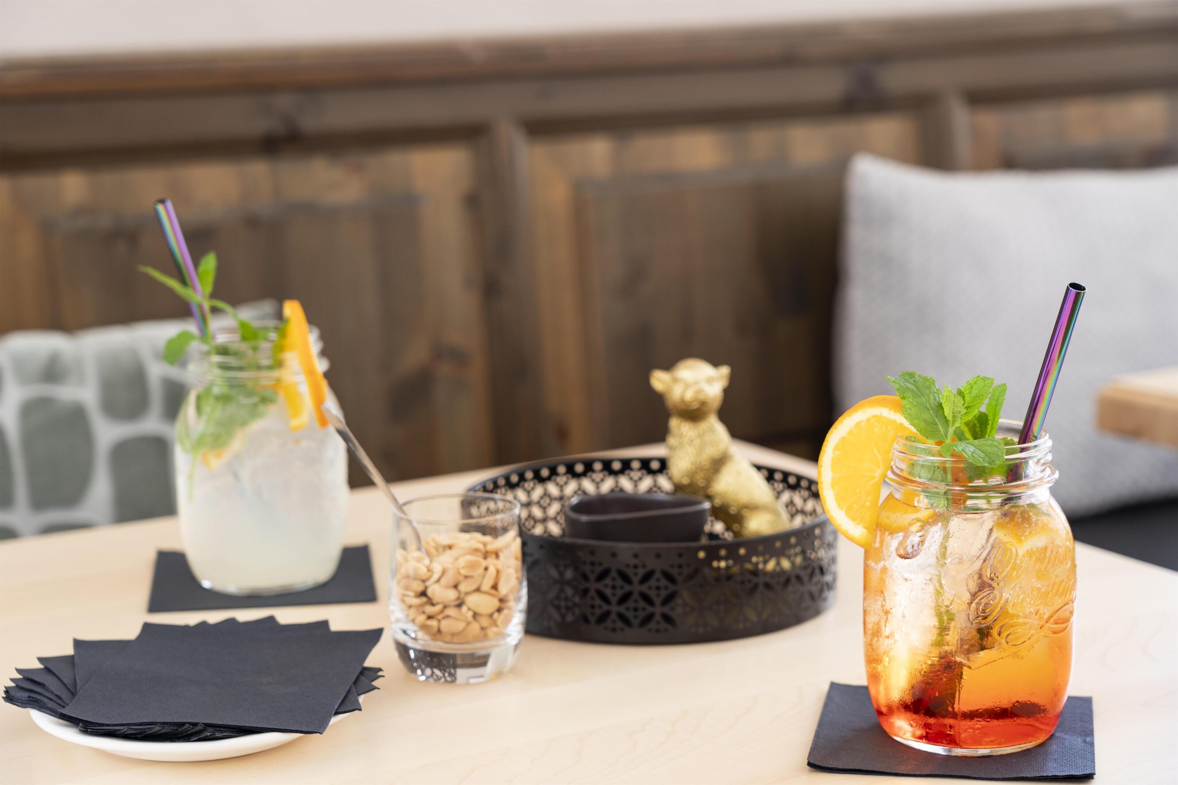 A table with two drinks, a small bowl of nuts, and a decorative bear figurine.