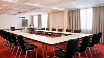 Ein Konferenzraum mit langem Tisch, schwarzen Stühlen, einer Whiteboard-Tafel und einer Projektionsleinwand.
