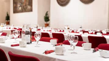 A banquet hall with tables set for dining, each with white tablecloths, red chairs, and clear glassware.