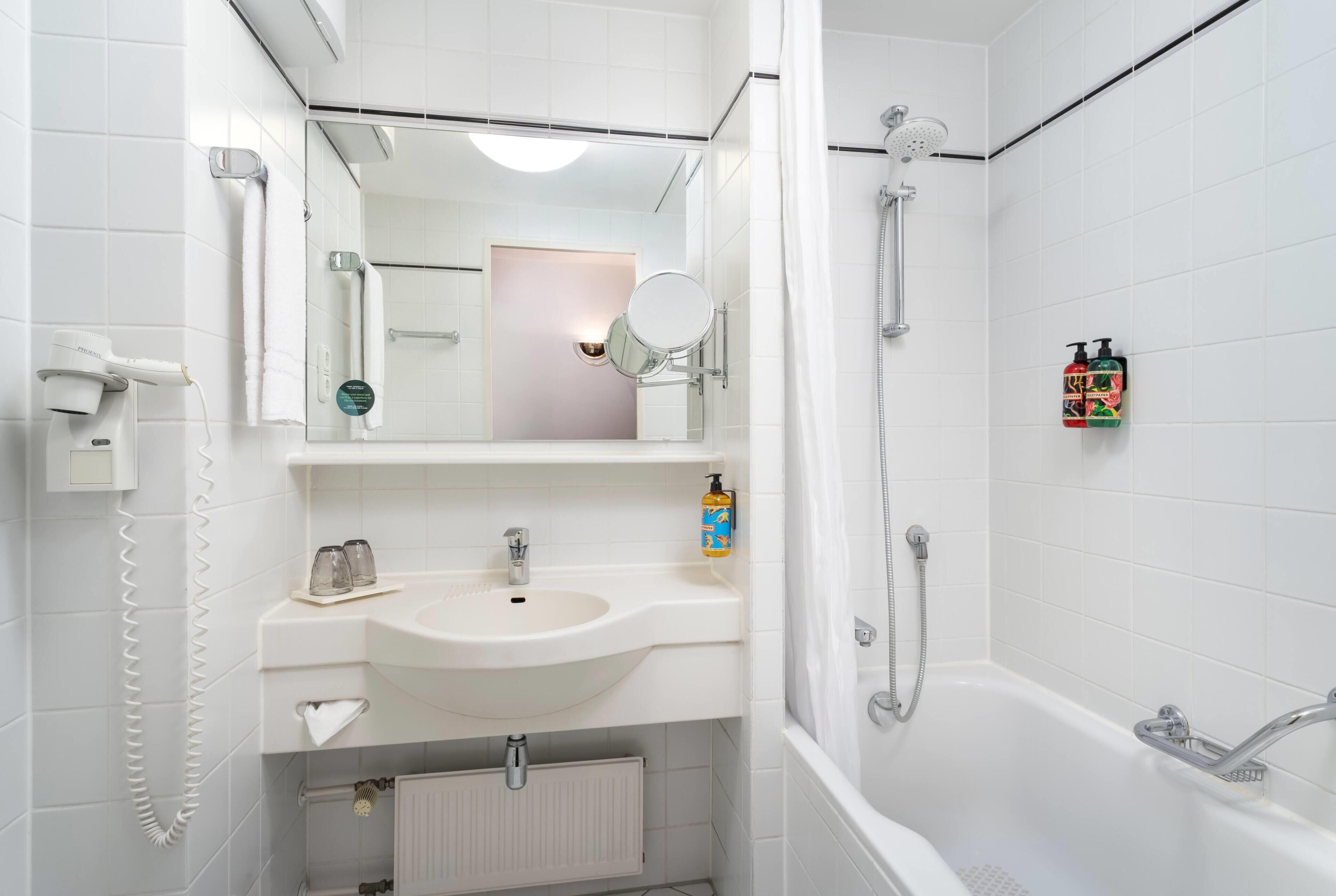 Un baño moderno con lavamanos, espejo y ducha blancos.
