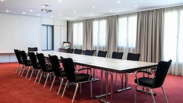 A conference room with a long table, black chairs, a projector, and a large window with curtains.
