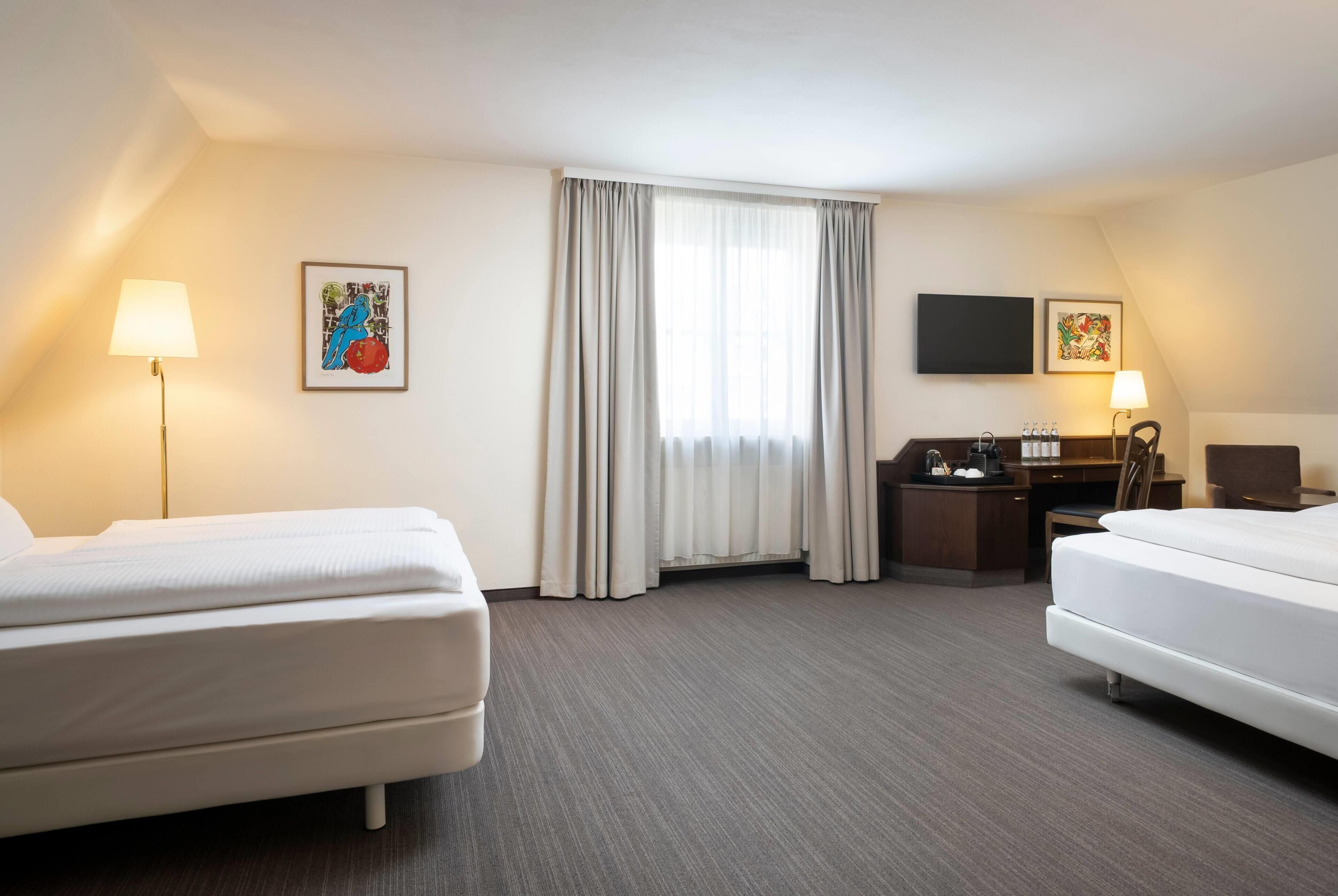 A hotel room with two beds, a desk, a chair, a TV, and a window with curtains.