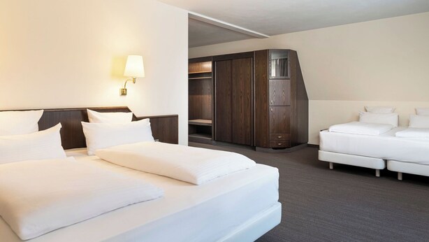 A hotel room with a large bed, a smaller bed, a wardrobe, and a desk.