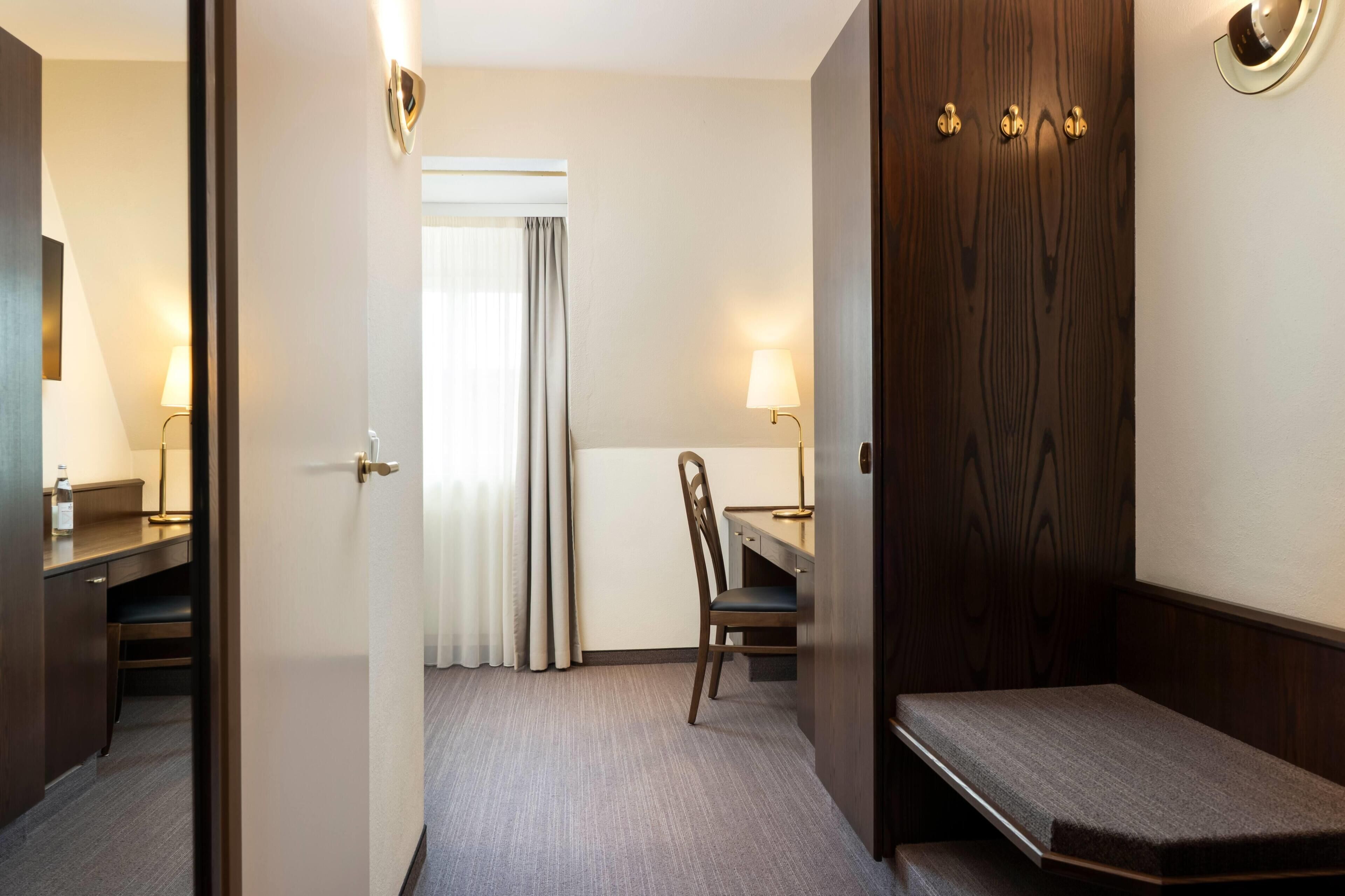 A hotel room with a bed, a desk, a chair, and a wardrobe.