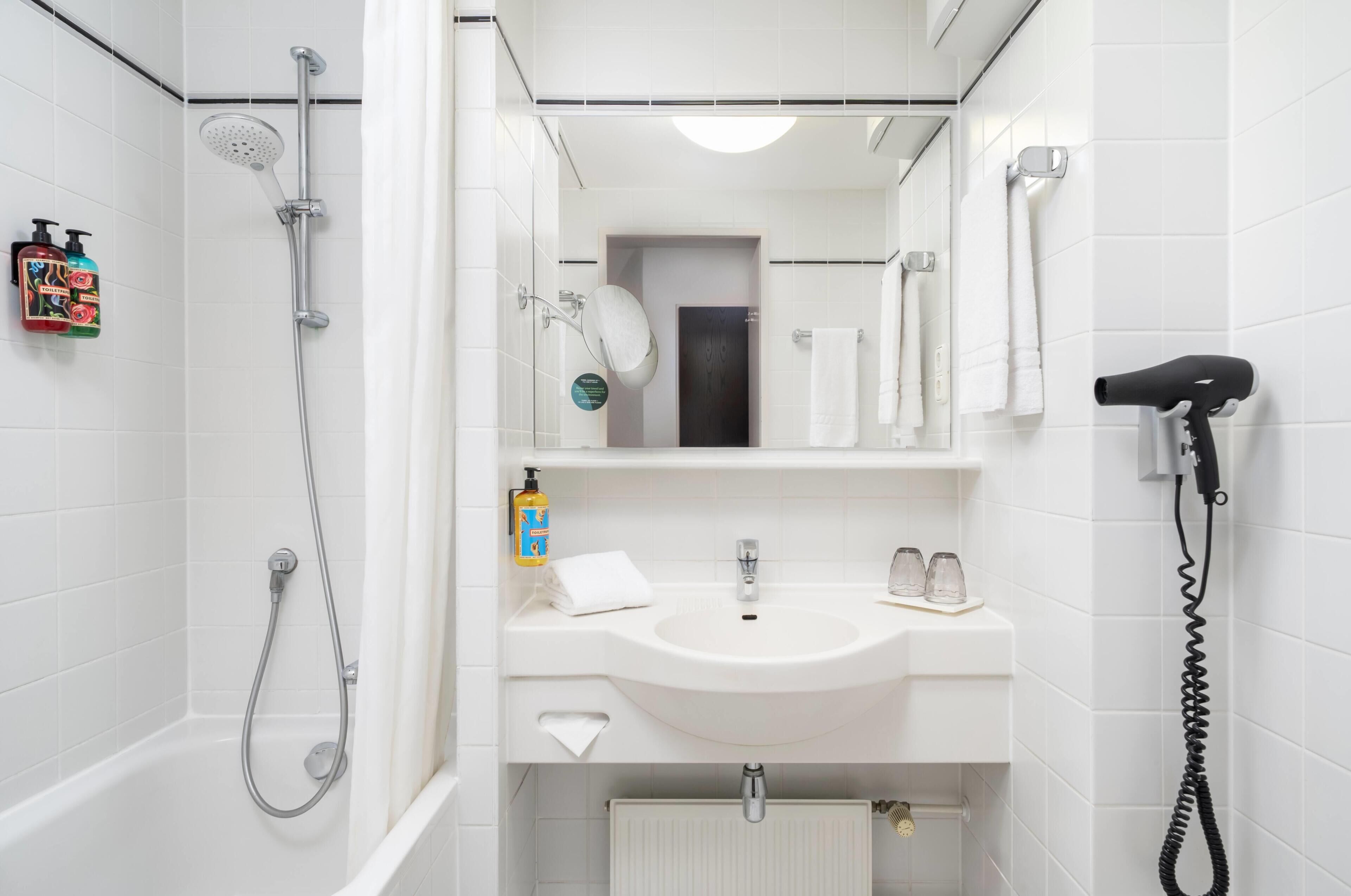 A bathroom with a shower, a sink, a mirror, a towel rack, and a hairdryer.