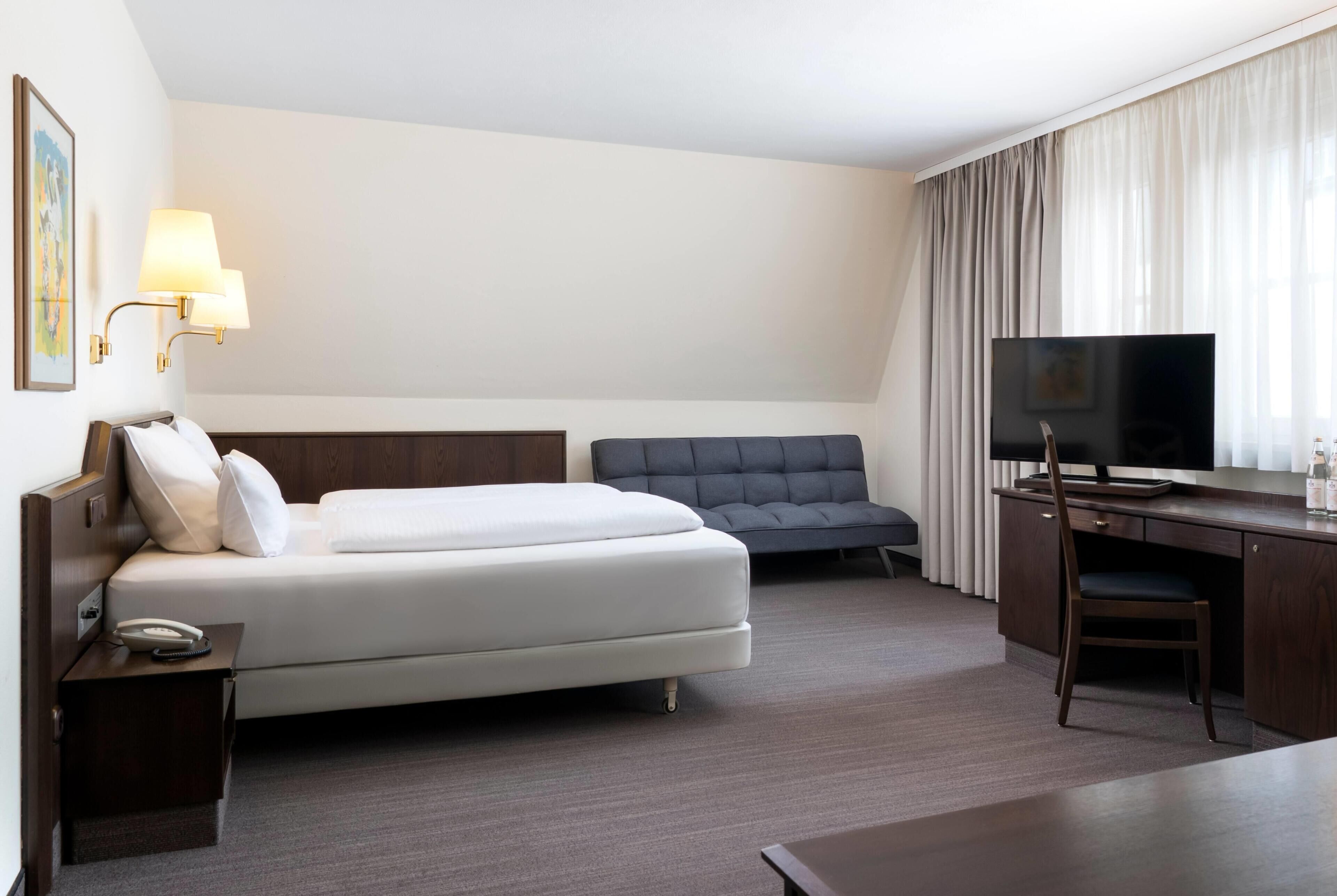 Een hotelkamer met een bed, een bureau met een televisie, een stoel en een lamp.