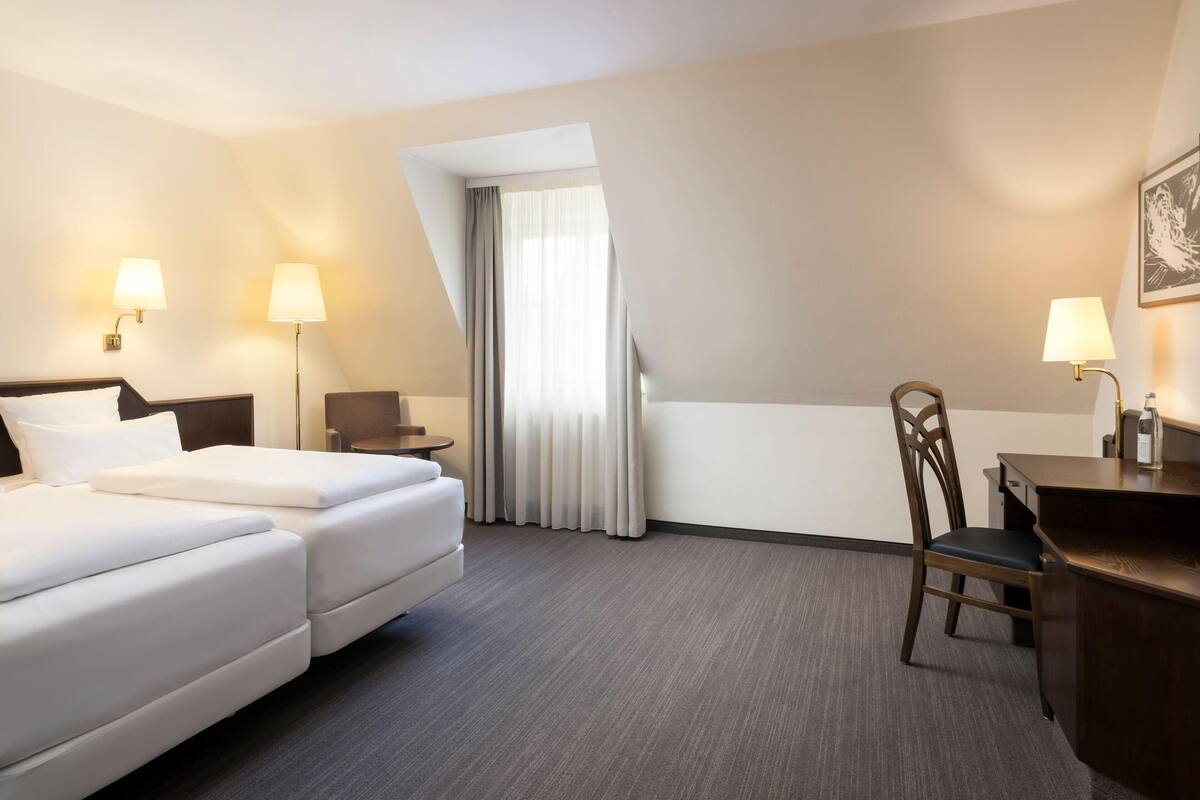 Una habitación de hotel con cama, escritorio, silla y dos lámparas.