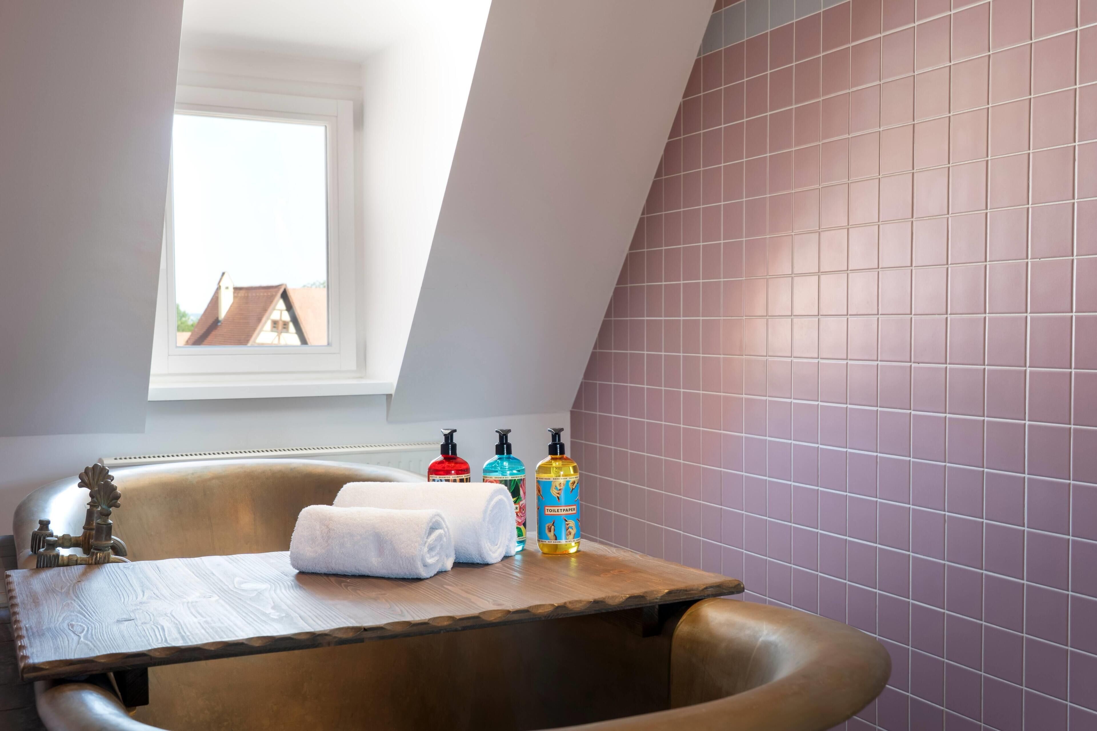 Ein Badezimmer mit einer Badewanne, einem Fenster und Pflegeprodukten auf einer Holztablett.