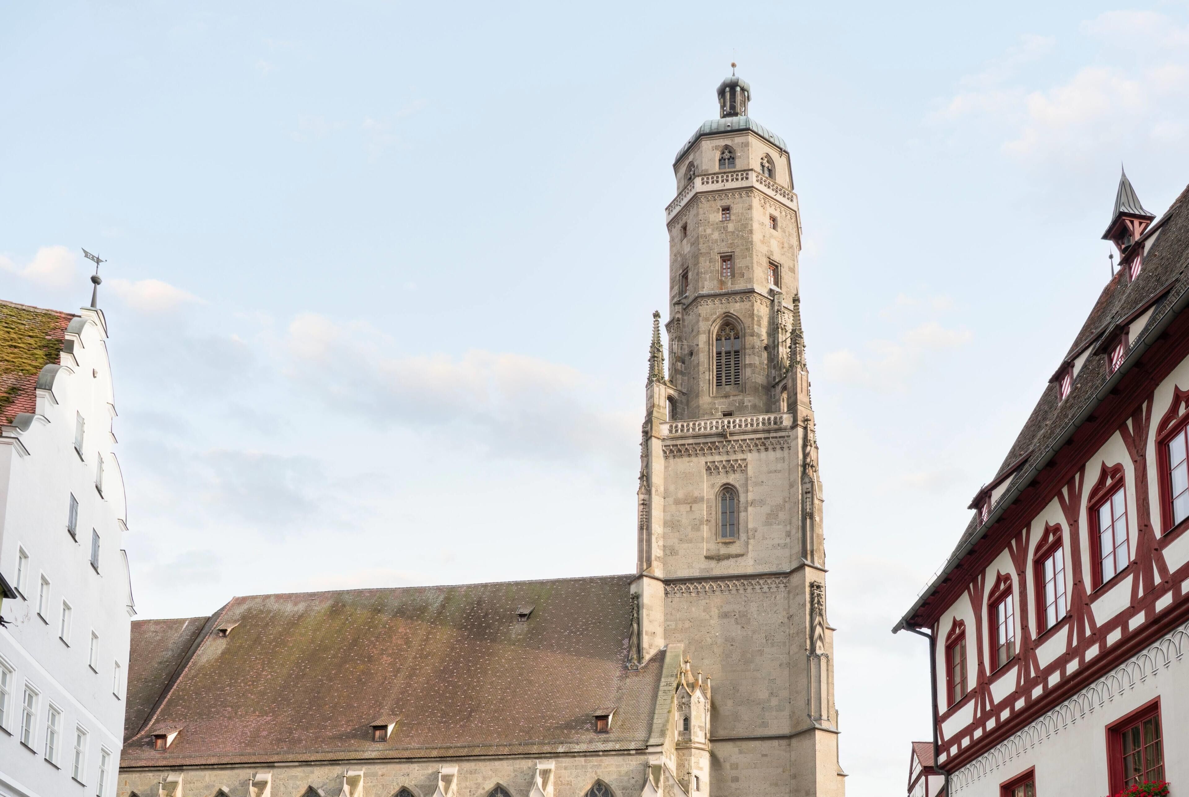 Ein historischer Turm mit einer Uhr, neben einem Gebäude mit traditioneller Fassade.