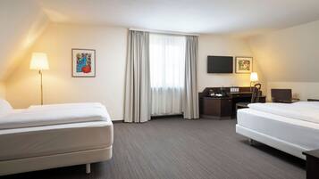 A hotel room with two beds, a desk, a chair, a flat-screen TV, and a window with curtains.