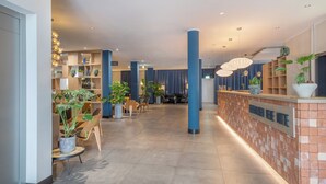 Eine Hotelhalle mit Rezeption, Sitzgelegenheiten und Pflanzenregalen.