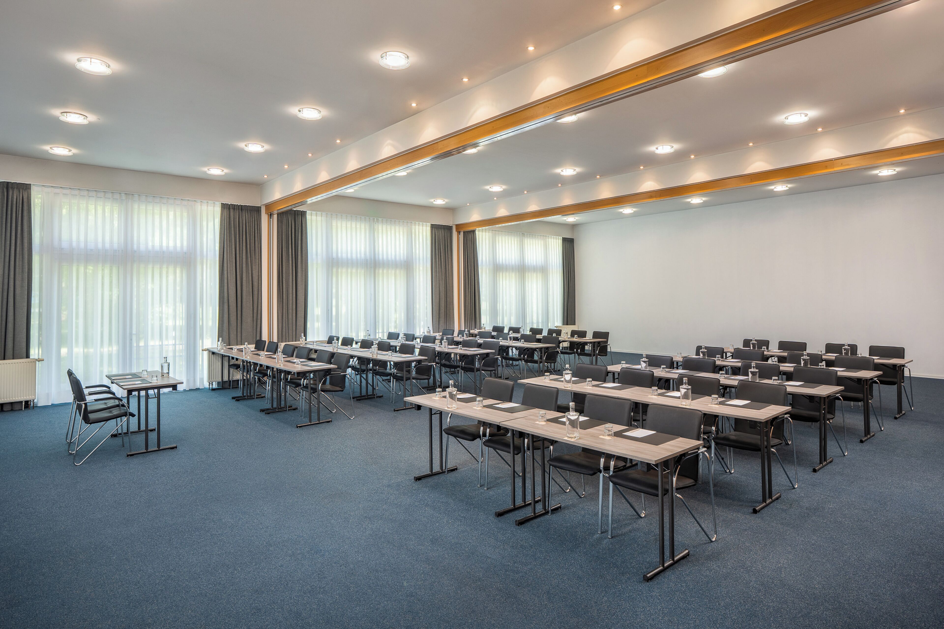 A conference room with multiple tables and chairs, large windows with curtains, and ceiling lights.