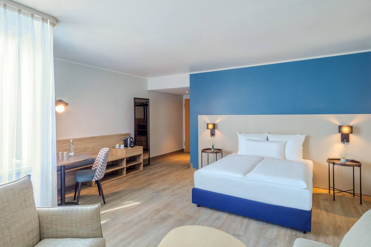 Habitación de hotel con una cama grande, un escritorio, una silla y una mesita de noche con lámpara.