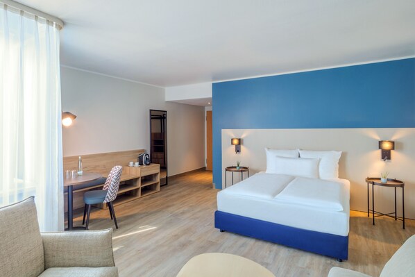 Habitación de hotel con una cama grande, un escritorio, una silla y una mesita de noche con lámpara.