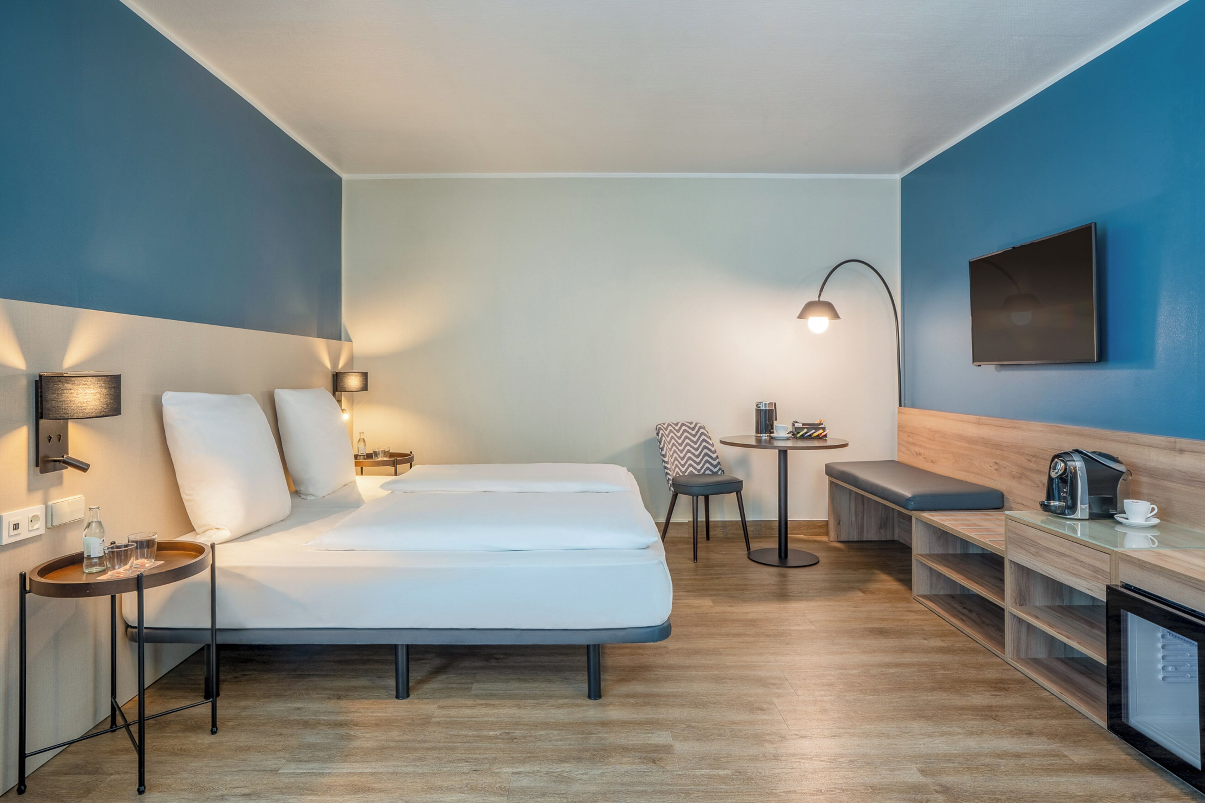 Een moderne hotelkamer met een groot bed, nachtkastjes, een zithoekje, een koffiezetapparaat en een flatscreen televisie.
