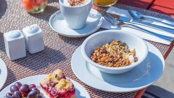 Ein gedeckter Tisch mit Frühstücksleckereien, darunter Brot, Obst, ein Getränk und eine Schüssel Müsli.