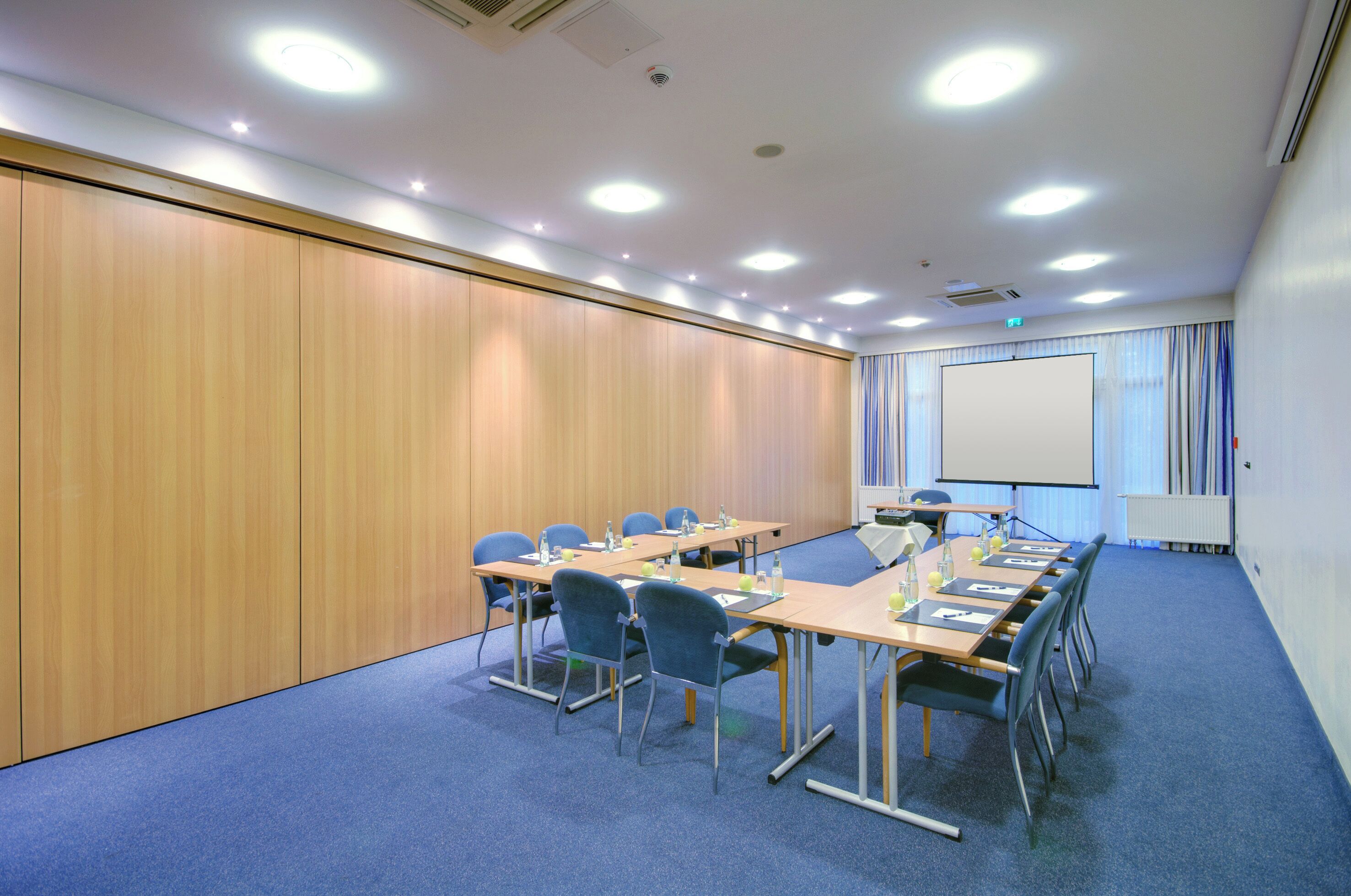 A conference room with a long table, chairs, a projector screen, and a whiteboard.