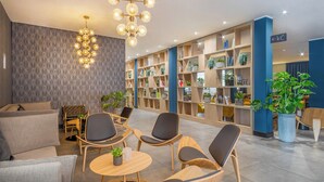 Eine moderne Lobby mit Sitzbereichen, einem großen Bücherregal und einer dekorativen Leuchte.