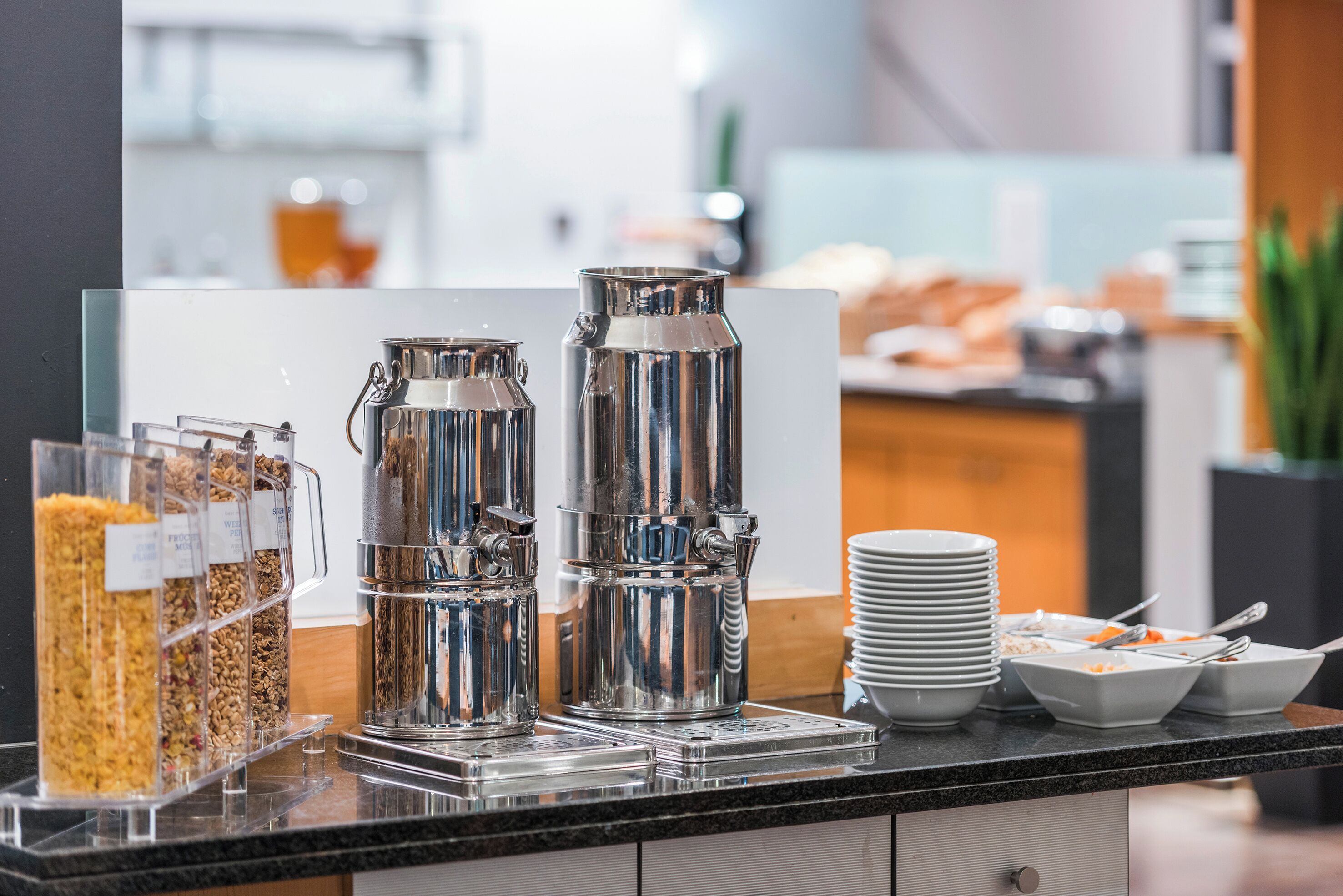 A buffet setup with clear containers of food and a stack of white plates on a black countertop.