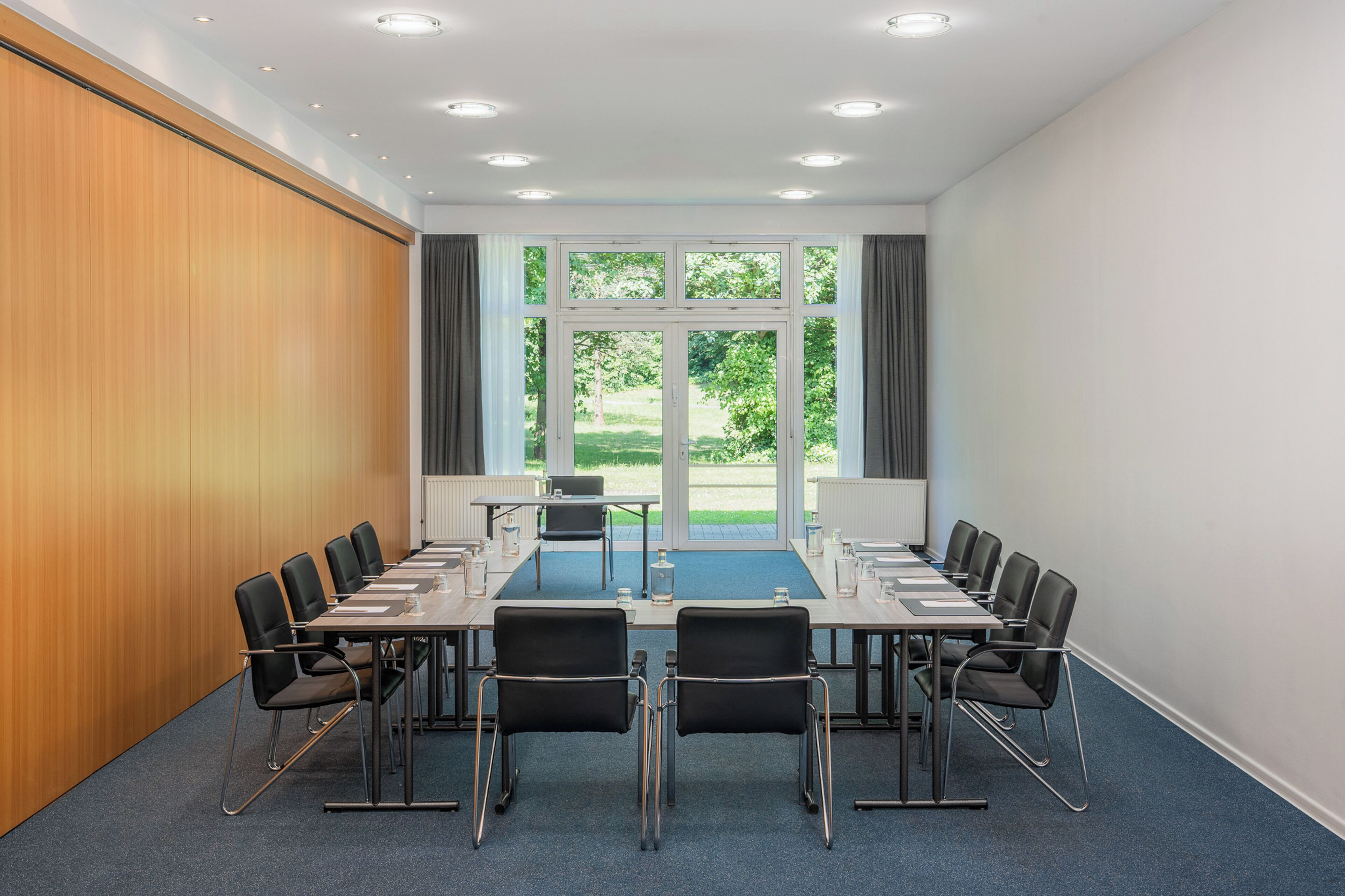 A conference room with a long table, chairs, and a view of greenery through large windows.